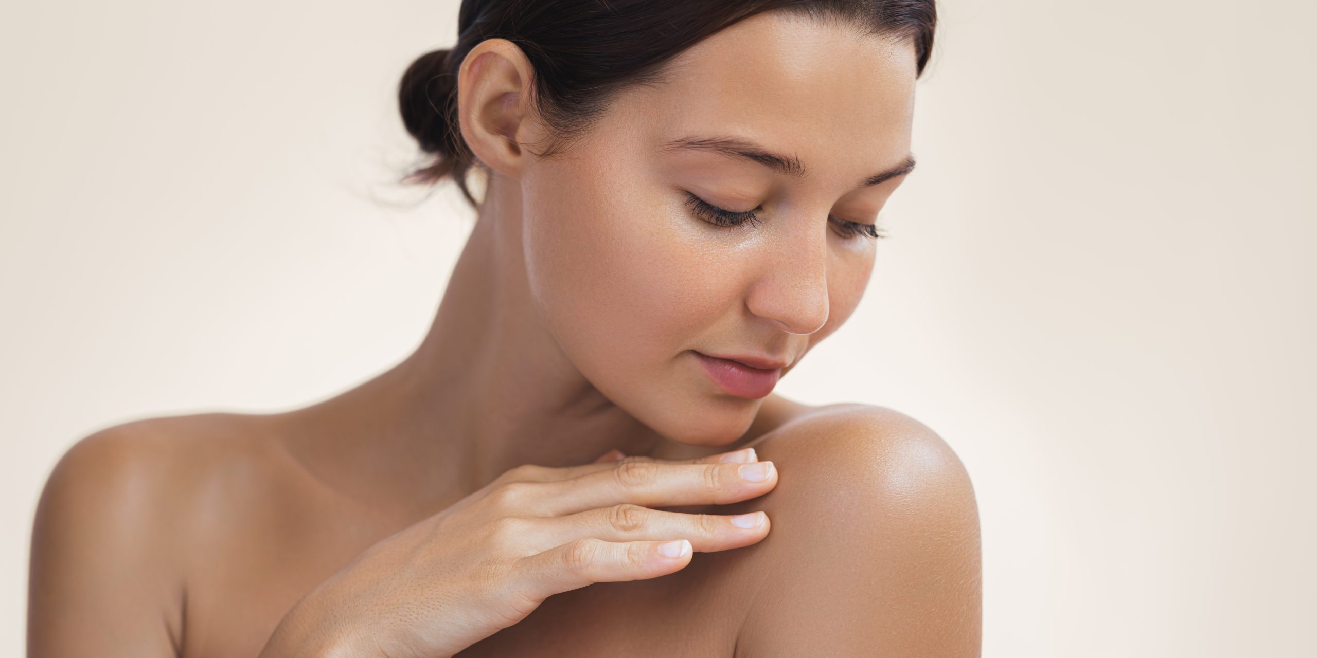 Skin Care and Cosmetics Concept Photo of Close-up Woman Perfect Hydrated Skin Beauty and skincare portrait with copy space for text. Crop photo of the woman with a beautiful young adult face touching her shoulder. A tender Asian girl with natural makeup enjoys glowing hydrated silky skin.